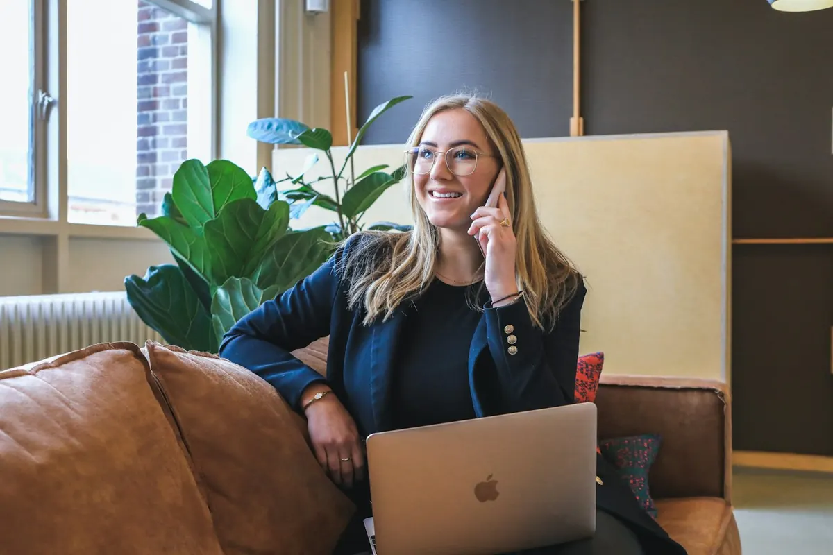 Mujer hablando por teléfono con el portátil sobre las rodillas, fuera del horario del taller